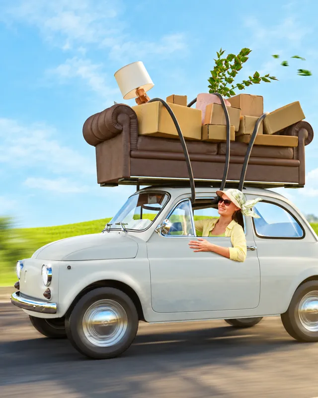Frau fährt in einem kleinen Auto mit Sofa und Kartons auf dem Dach als Sinnbild für den Wechsel der E-Commerce-Plattform